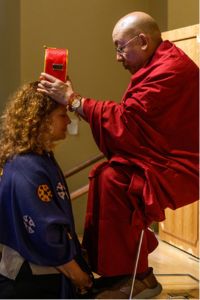 The Nechung Oracle places a ceremonial object on a woman's head as part of a cultural ritual.